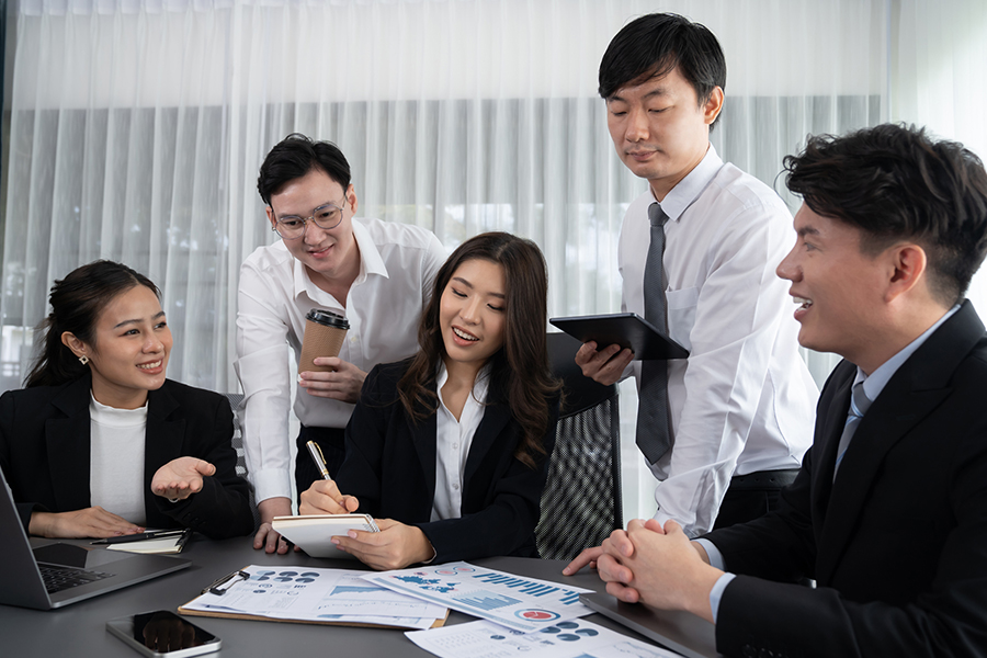 A team of professionals collaborating in an office, discussing charts and graphs, representing an IT services provider in Japan