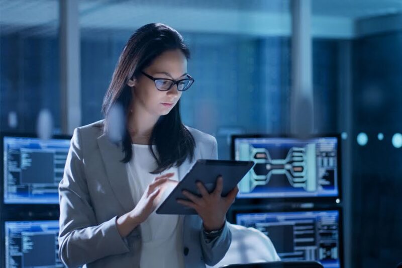 A woman in a business suit uses a tablet in a high-tech office, symbolizing IT security and data management