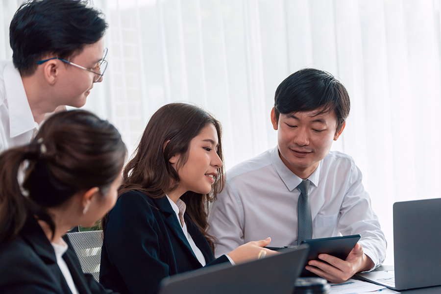 Business professionals in Japan discussing japan wi-fi design services, using a tablet and laptops to plan seamless connectivity