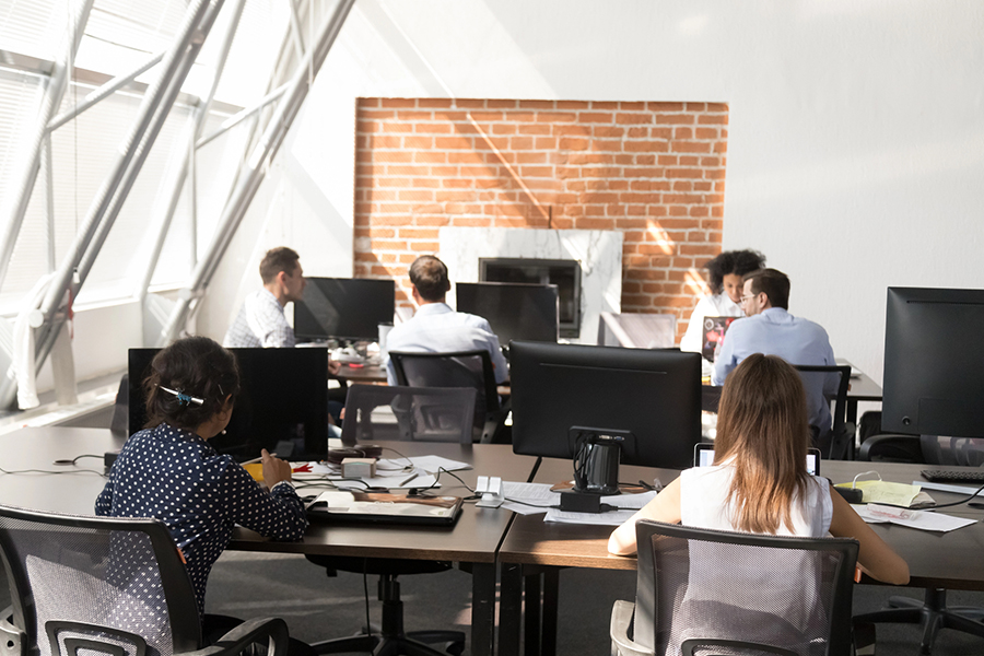 Professionals working in an open office space with computers and collaborative discussions, representing an IT company in Japan.